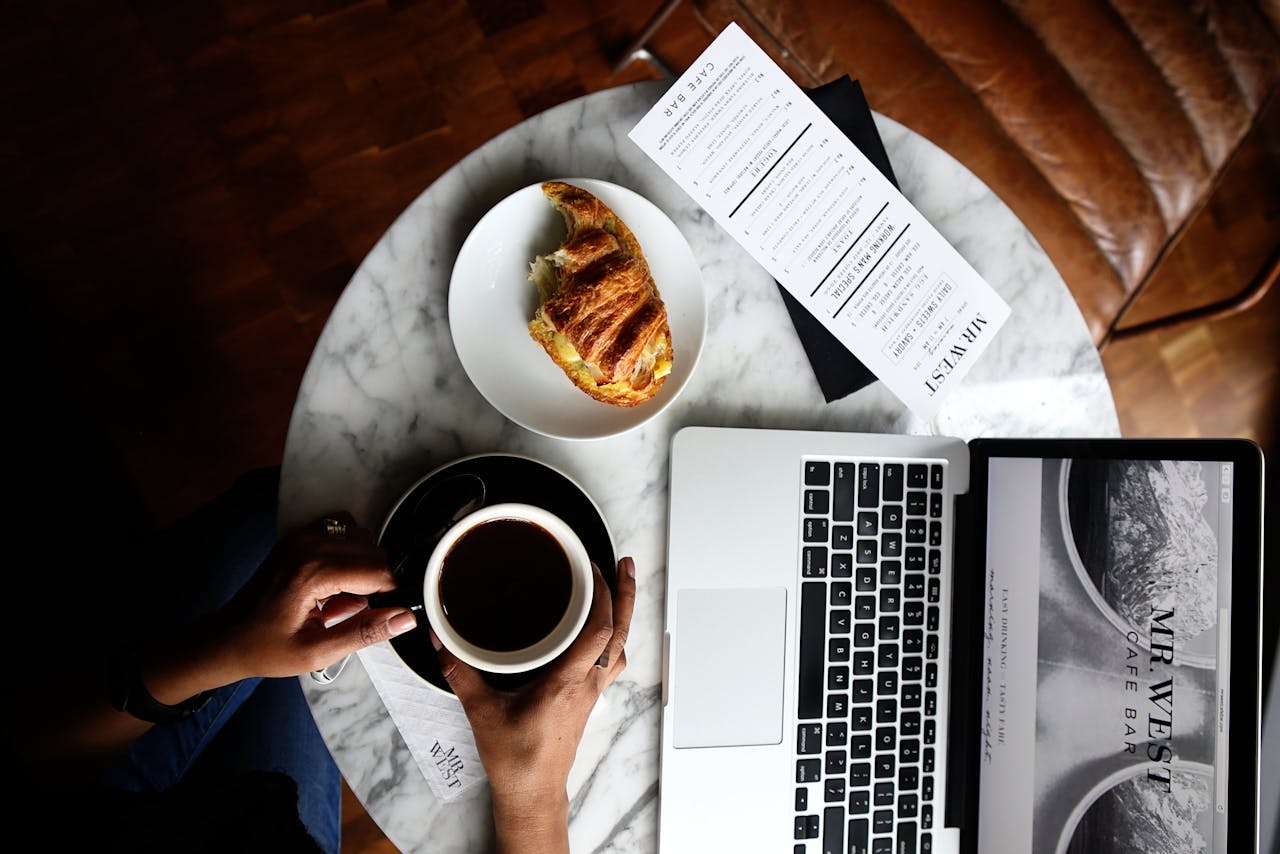 Top view of a marble table with coffee, croissant, and laptop perfect for a productive morning.